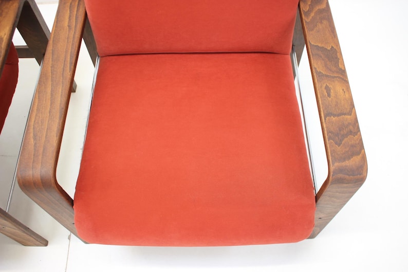 May include: Close-up of a mid-century modern chair with a vibrant orange seat and back. The chair features a wooden frame with a dark finish and curved armrests. The design is simple and elegant, showcasing a retro aesthetic.