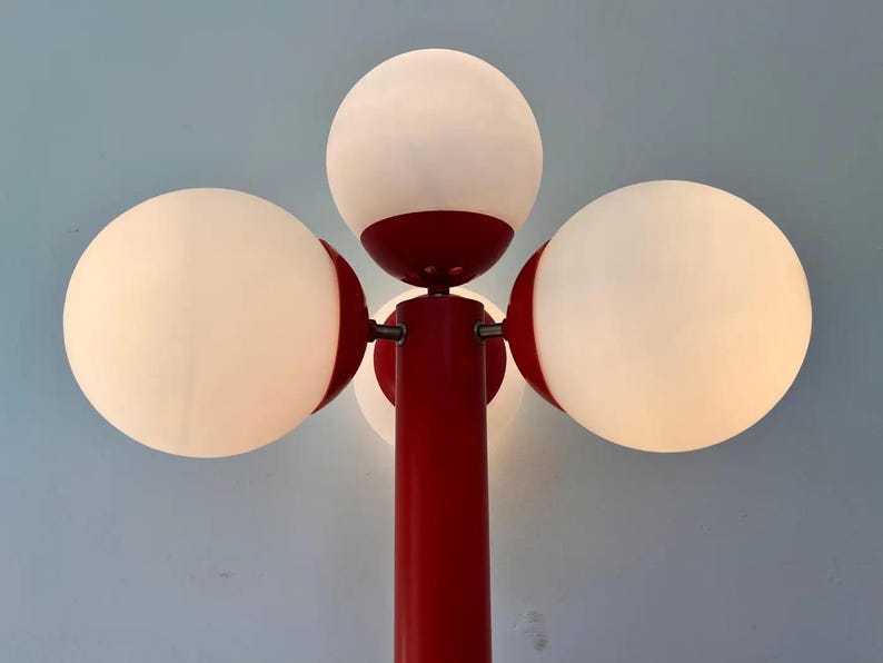 May include: A red and white floor lamp with four spherical white light fixtures. The lamp has a central red pole and red accents around the lights. The background is a light blue.