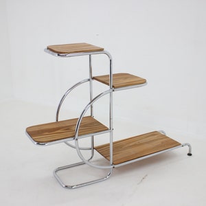 May include: A chrome plant stand with four wooden shelves. The stand has a unique design with curved metal supports.