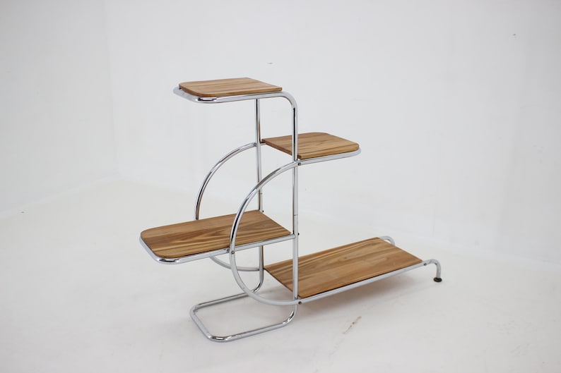 May include: A chrome plant stand with four wooden shelves. The stand has a unique design with curved metal supports.