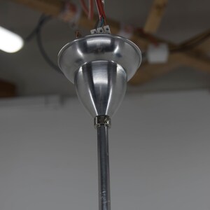 May include: Close-up of a silver metal ceiling fixture with a hook and wires attached. The fixture is hanging from a ceiling.