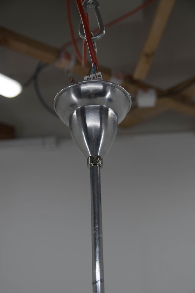 May include: Close-up of a silver metal ceiling fixture with a hook and wires attached. The fixture is hanging from a ceiling.