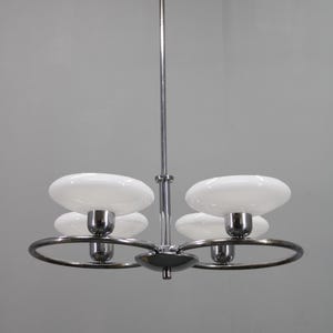 May include: A chrome and white glass chandelier with four lights. The fixture has a central rod and circular arms holding the lights. Each light has a white, saucer-shaped shade. The overall design is sleek and modern.