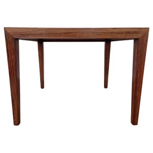 May include: A rectangular wooden table with a dark brown finish. The table has four legs, with the two front legs wider at the base and tapering upwards. The top of the table is a solid, rectangular piece of wood.