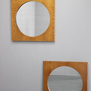 Puede incluir: Dos espejos redondos con marco de madera. El espejo superior es ligeramente más pequeño que el espejo inferior. Ambos espejos tienen un marco de madera marrón claro.