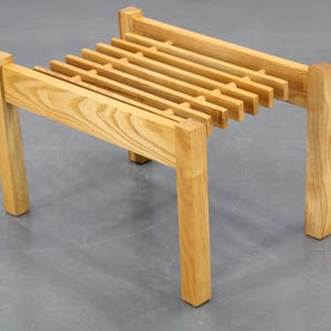 May include: A wooden stool with a slatted top and four legs. The stool is made of light brown wood and has a simple, modern design.