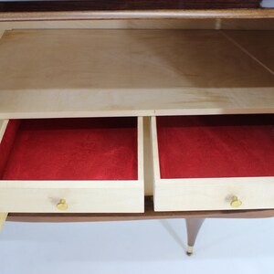 May include: A wooden cabinet with two drawers and a shelf. The drawers are open and lined with red felt. The cabinet has a light wood finish and brass hardware.