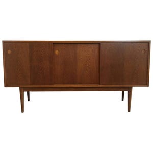 May include: A mid-century modern wooden sideboard with a warm brown finish. It features two sliding doors in the center and two hinged doors on the sides. The doors have circular handle cutouts. The sideboard is supported by four tapered legs.