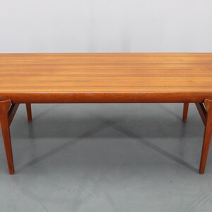 May include: A rectangular, mid-century modern coffee table. The table is made of wood with a warm, reddish-brown finish. It has a rounded edge and angled legs. The table measures approximately 60 inches long, 20 inches wide, and 16 inches high.