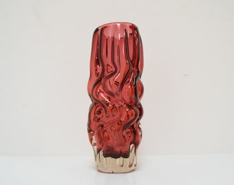 May include: A red glass vase with a wavy, textured design. The vase has a clear glass base.