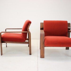May include: Two mid-century modern armchairs. The chairs have a wooden frame and are upholstered in a vibrant red fabric. The design features clean lines and a minimalist aesthetic, perfect for a living room or lounge area.