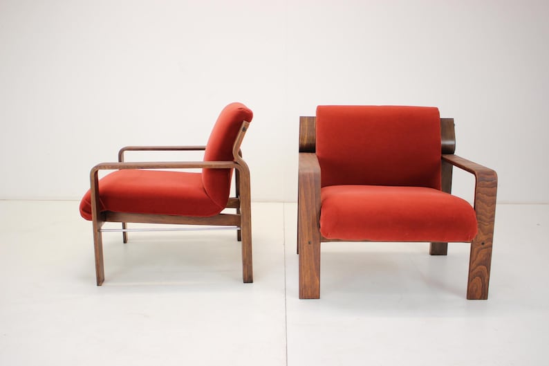 May include: Two mid-century modern armchairs. The chairs have a wooden frame and are upholstered in a vibrant red fabric. The design features clean lines and a minimalist aesthetic, perfect for a living room or lounge area.