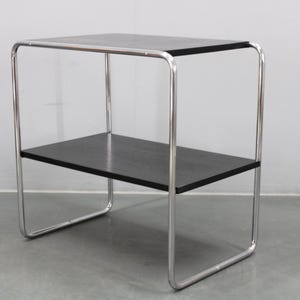 May include: A contemporary side table featuring a black top and shelf, supported by a chrome-finished, tubular steel frame. The table's design is minimalist, with a rectangular shape and two tiers. The dimensions are suitable for various interior settings.
