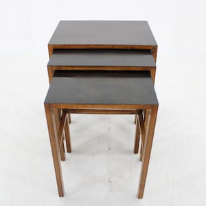 May include: A set of three nesting tables with dark wood tops and light wood frames. The tables are stacked on top of each other.