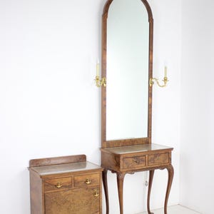 Könnte beinhalten: Ein Vintage-Frisiertisch-Set aus Holz mit einem hohen, gewölbten Spiegel, zwei Messingkerzenhaltern und einem kleinen Schrank. Der Frisiertisch hat zwei Schubladen und eine Glasplatte. Der Schrank hat eine Tür und zwei Schubladen.