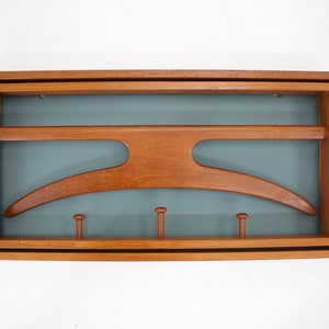 Könnte beinhalten: Ein Wand-Kleiderständer aus Holz mit einem gebogenen Kleiderbügel und vier Haken. Der Kleiderständer hat einen hellblauen Hintergrund und ist aus Naturholz gefertigt.