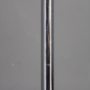 May include: A vertical, shiny, chrome-colored metal pole. The pole has a smooth, reflective surface with minor imperfections. The background is a solid, neutral gray.