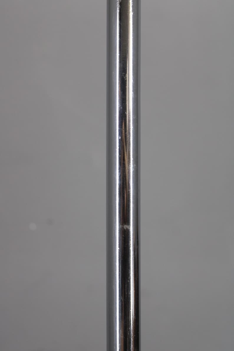 May include: A vertical, shiny, chrome-colored metal pole. The pole has a smooth, reflective surface with minor imperfections. The background is a solid, neutral gray.
