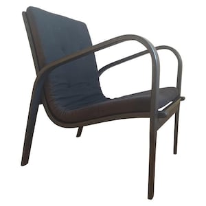 May include: A dark grey armchair featuring a curved wooden frame with integrated armrests. The seat and backrest consist of a single continuous upholstered cushion with tufted detailing, supported by four slender, angled wooden legs.