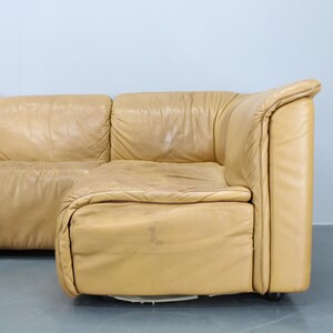 May include: A large, tan leather sectional sofa with a modular design. The sofa has a curved, rounded shape and is made of multiple pieces that can be arranged in different configurations.