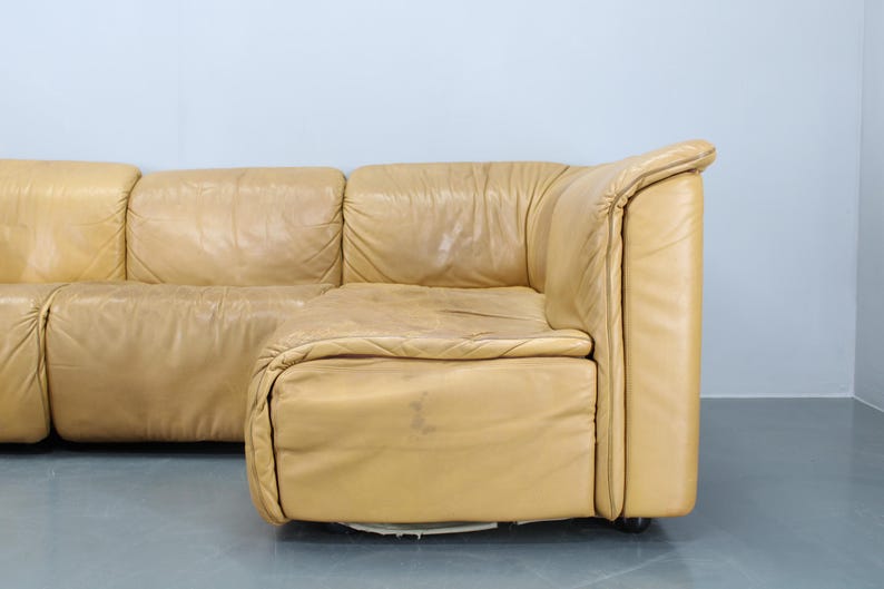May include: A large, tan leather sectional sofa with a modular design. The sofa has a curved, rounded shape and is made of multiple pieces that can be arranged in different configurations.