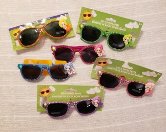 May include: Five pairs of colorful, jeweled sunglasses for kids, each with a mermaid charm. The sunglasses are displayed on their packaging, which features a sun and clouds. The packaging also includes the text "Kid's Sunglasses" and "Lunettes de Soleil pour enfant".