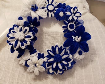 May include: A blue and white wreath made of pipe cleaners, featuring a variety of flower shapes. The wreath is decorated with blue and white flowers.