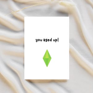 以下が含まれることがあります： 「you aged up!」という黒い文字と緑色のダイヤモンドの形が書かれた白いカードです。