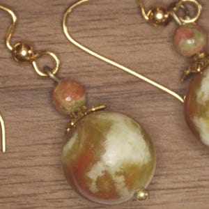 Può includere: Orecchini pendenti color oro con grandi perline marmorizzate nei toni dell'arancione, crema e verde. Gli orecchini hanno una piccola perla rotonda sopra la perla più grande e un gancio color oro.