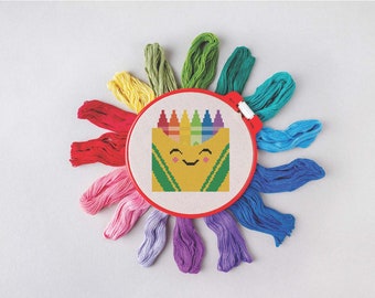 May include: A colorful embroidery hoop with a cross-stitch design of a smiling crayon box. The hoop is surrounded by spools of embroidery floss in various colors.