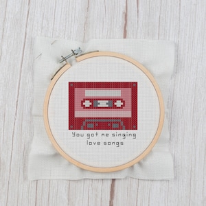 Könnte beinhalten: Ein Kreuzstich-Stickrahmen mit einem roten Kassettenband-Design und dem Text "You got me singing love songs".