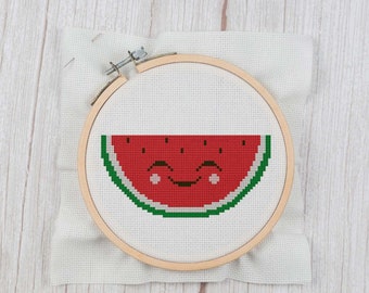 May include: A cross-stitch embroidery hoop with a red watermelon design. The watermelon has a smiling face with black eyes and a green rind.