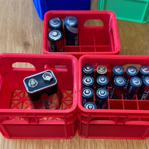 May include: Three red plastic crates with compartments for storing batteries. The top crate has two AA batteries, the middle crate has one 9-volt battery, and the bottom crate has 15 AA batteries.