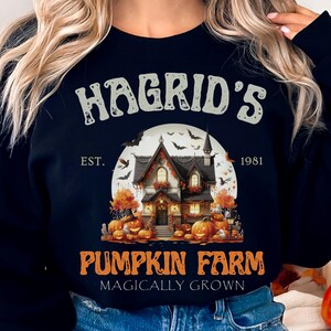 May include: Black sweatshirt with a Halloween design. The graphic shows a house, pumpkins, bats, and the text "Hagrid's Pumpkin Farm" with "Magically Grown" underneath. The year "1981" is also included in the design.
