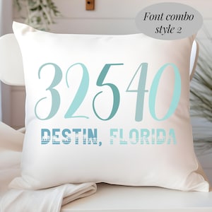 May include: White cushion featuring the text "32540 DESTIN, FLORIDA" in shades of blue. The cushion has a soft texture and is likely made of cotton or a similar fabric. The text is in a stylish font.