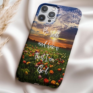 May include: A phone case with a sunset and field of flowers background. The text "Be still and know that I am God" is printed on the case.
