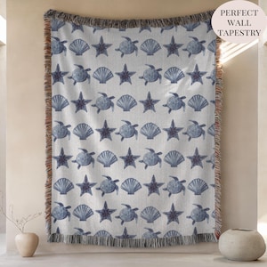 May include: A white woven throw blanket with a repeating pattern of blue seashells, starfish, and turtles. The blanket has a fringed edge and the text "PERFECT WALL TAPESTRY" in a pink circle.