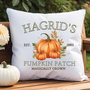May include: White square pillow with the text "Hagrid's Pumpkin Patch" and a watercolor illustration of pumpkins and fall foliage. The pillow has the text "Est. 1962" and "Magically Grown".