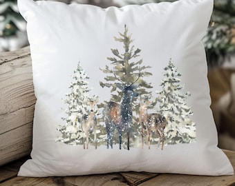 May include: White throw pillow with a watercolor design of a snowy forest scene. The design features three pine trees with a deer and two fawns standing in front of them.