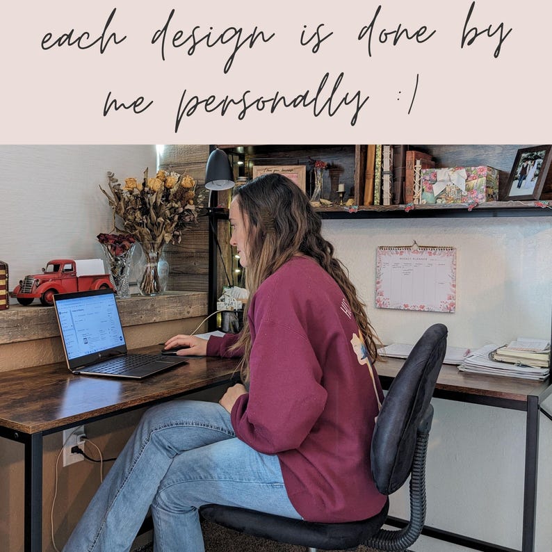 Op de afbeelding: Een persoon zit aan een bureau met een laptop, een rood vrachtwagenfiguurtje en een vaas met gedroogde bloemen. De persoon draagt een bordeauxrood sweatshirt en een blauwe jeans. De tekst "each design is done by me personally" is zichtbaar in de afbeelding.
