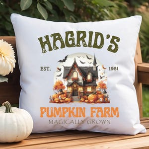 Peut inclure: Coussin carré blanc avec un motif sur le thème d'Halloween. Le motif présente le texte "Hagrid's Pumpkin Farm" avec une illustration d'une maison effrayante, de citrouilles et de chauves-souris. Le texte "Est. 1981" est également inclus.