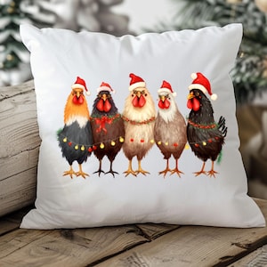 May include: White square cushion featuring a watercolour illustration of five chickens wearing Santa hats and festive lights. The chickens have various colours of feathers, including orange, black, and brown. A Christmas-themed decorative cushion.