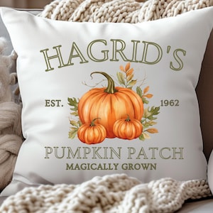 May include: White decorative pillow with a watercolor illustration of pumpkins and fall foliage. The text on the pillow reads "Hagrid's Pumpkin Patch Magically Grown Est. 1962". The design features a large orange pumpkin and two smaller pumpkins.