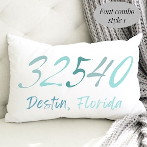May include: White rectangular pillow with the text "32540 Destin, Florida" in shades of blue. The pillow is on a white surface with a gray knitted blanket in the background. The text "Font combo style 1" is in the upper right corner.