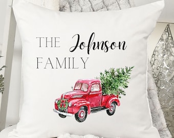 May include: White decorative pillow with the text "THE Johnson FAMILY". The pillow features a watercolor illustration of a red vintage truck carrying a Christmas tree. A festive wreath adorns the front of the truck.