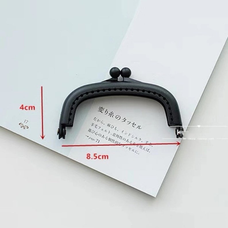 May include: Black metal purse frame with two round knobs. The frame measures 8.5 inches wide and 4 inches tall.