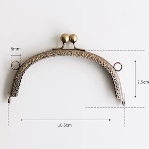 May include: A gold-toned metal purse frame with an ornate design. The frame measures 7.5 inches tall and 16.5 inches wide.
