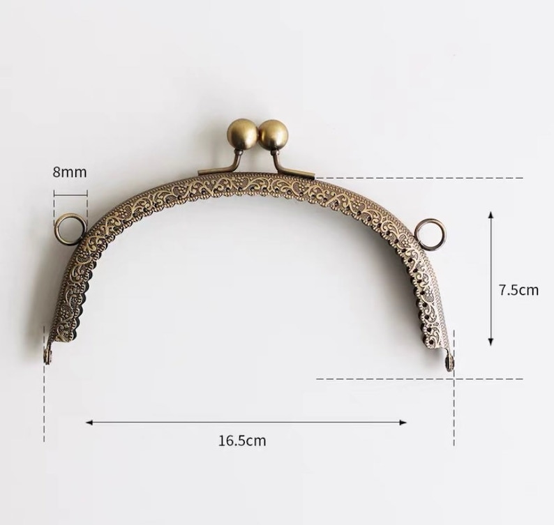 May include: A gold-toned metal purse frame with an ornate design. The frame measures 7.5 inches tall and 16.5 inches wide.