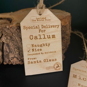 May include: A wooden Christmas gift tag with the text "Special Delivery for Callum" and a checkbox marked "Nice". The tag is decorated with a stamp that says "Lapland The North Pole" and "From: Santa Claus".