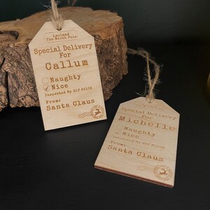 May include: Two wooden Christmas gift tags with a rustic design. The tags are brown and have a white string attached. The tags have the text "Special Delivery" and "Inspected By Elf #2108" on them. One tag is for Callum and the other is for Michelle. Both tags have a checkbox for "Naughty" and "Nice" with the "Nice" box checked.